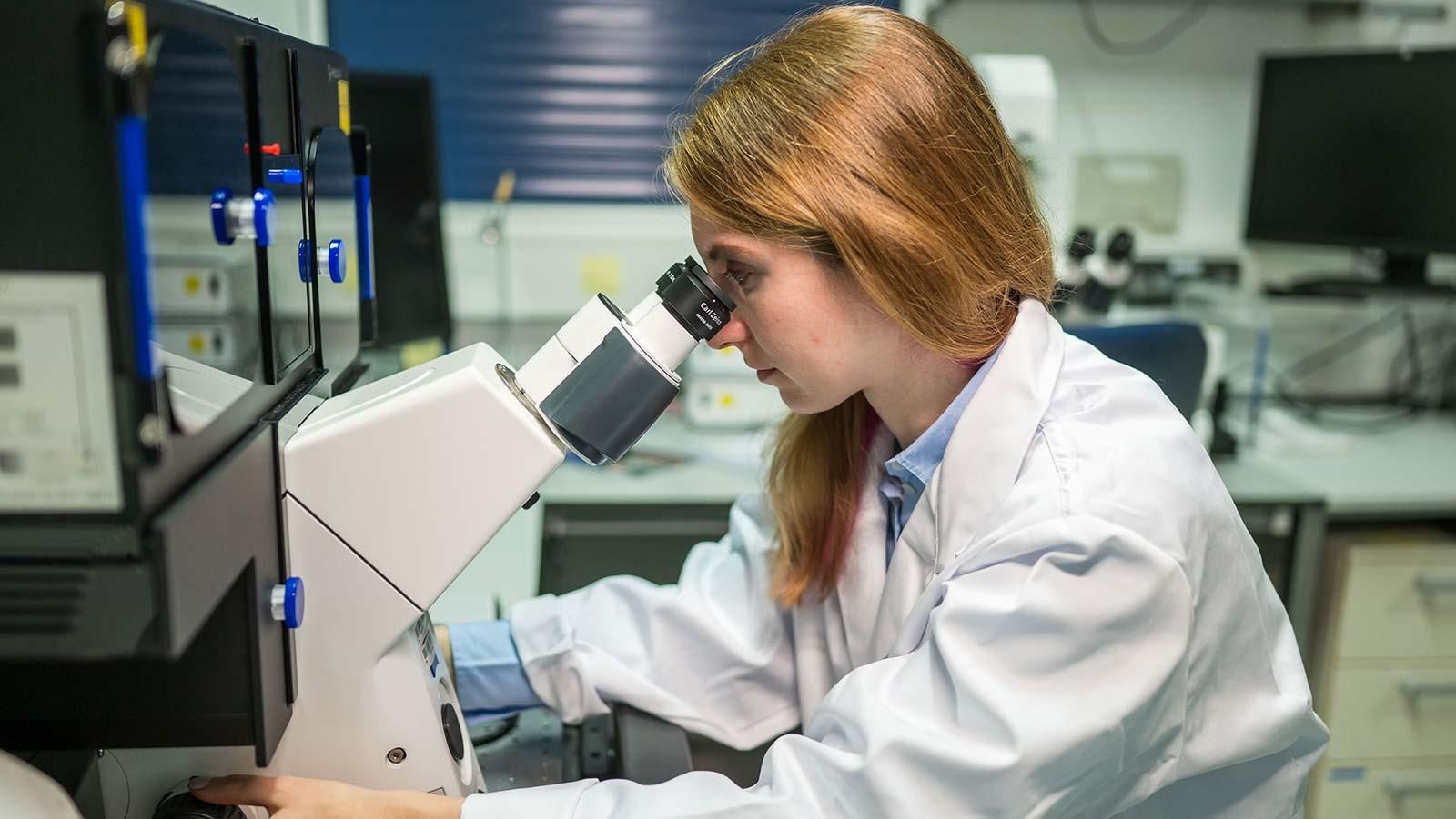 Forscherin am Sanofi BioCampus sitzt vor einem Mikroskop in einem Labor