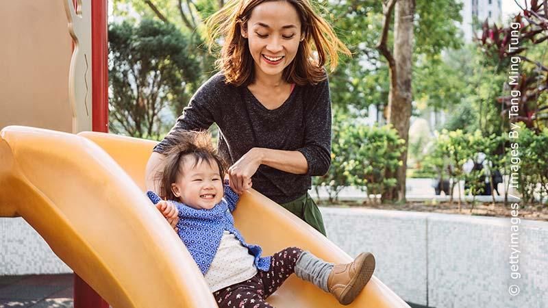 Kleinkind spielt auf einer Rutsche mit seiner Mutter
