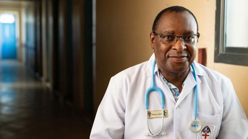 Dr. Yohana Mokiwa, ein lächelnder Mann mittleren Alters mit kurzen Haaren und Brille, in Arztkleidung.